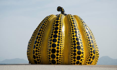 A giant yellow and black polka dotted pumpkin sculpture in a coastal location in Japan.