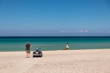 A man with a small beach vehicle flattens sand on a beach in Italy.
