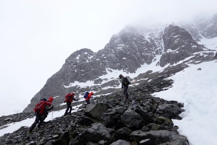 Four members of a rescue team climb a rocky incline patched with snow