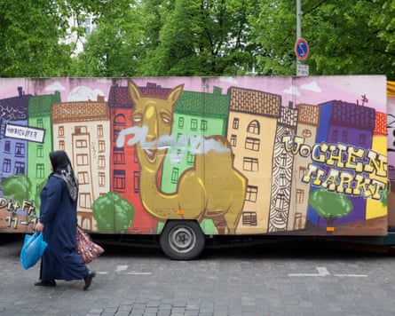 A woman walks past a large mural advertising a market.