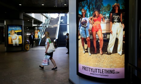 A shopper passes billboards for Boohoo and for Pretty Little Thing at Canary Wharf DLR station in London