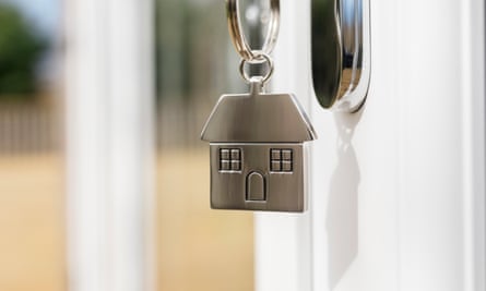 House key on a house shaped silver key ring in the lock of a door