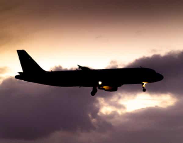 Silhouette of a landing aircraft with a cloudy background after the sunset.