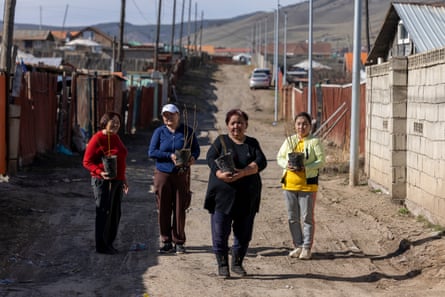 Four women in an unmade Ulaanbaatar street holding plant pots.
