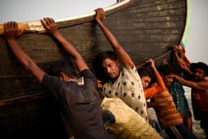 Refugiados Rohingya empurram um barco de pesca do mar na praia de Shamlapur