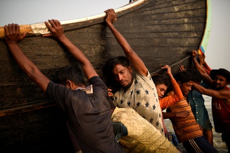 Rohingya refugees push a fishing boat from the sea at Shamlapur beach