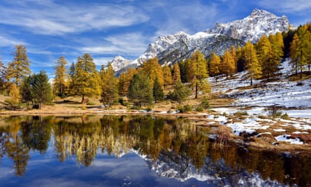 Snow-covered mountains and autumnal forest reflected in the Lai Nair, Tarasp, Switzerland.