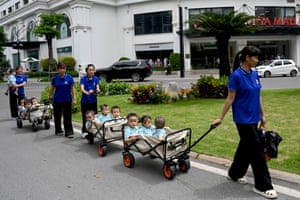 Women pull carts carrying toddlers along a residential street
