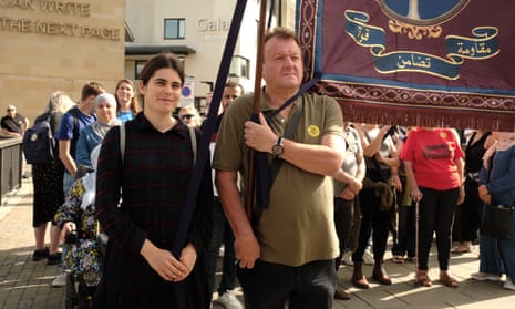 a middle-aged man carrying a banner in a procession, a younger woman walking alongside him