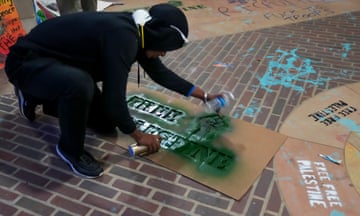 A person spraypaints a protest sign at UCLA