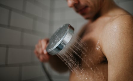 A man washes his chest with a shower headA man holds a shower head close to his chest and neck and washes his body.