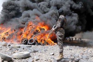 A soldier holding a gun looks at a huge fire billowing dark smoke