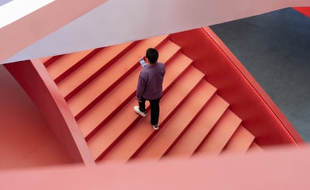 A young Asian man, dressed in casual attire, is walking up the steps of a vibrant red building – a scene of modern urban life.