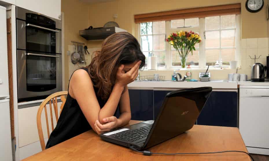 woman in despair sitting at kitchen table with laptop
