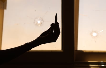 A silhouette of a large-calibre bullet held up in front of a window with bullet holes