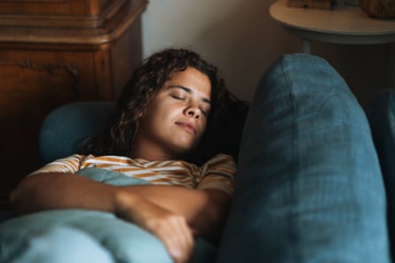 A young woman with curly hair taking a nap on a blue sofa.