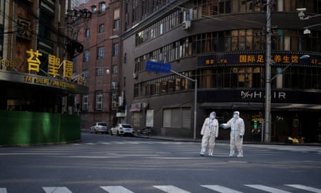 Workers in protective suits keep watch on a street during a lockdown in Shanghai
