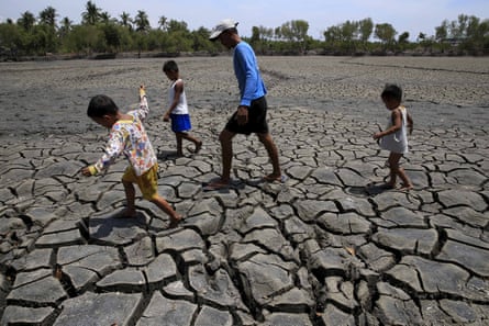 A man and some children walk across cracked, dry earth