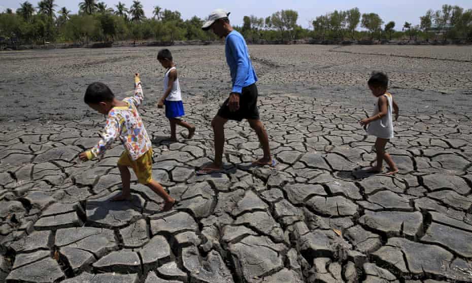 A father and his children walk over a dried out fishery near Manila