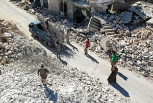 People collect scrap steel rods from the rubble after an aerial bombardment in Ihsim, Syria