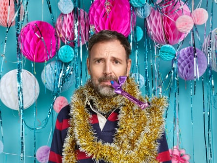 Tim Dowling wearing gold tinsel round his neck and blowing a party hooter, with a pained expression on his face