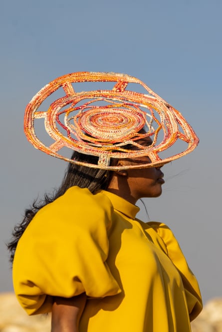 A woman in a yellow dress wears a woven head piece