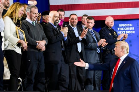 A man in a dark suit and blue tie reaches his right hand out to shake a woman’s hand