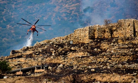 A firefighting helicopter drops water to extinguish flames during a wildfire near the archaeological site of Mycenae.