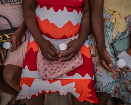 A view of three women’s laps from above as they sit holding urine sample bottles