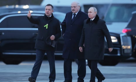 Russian President Vladimir Putin, right, and Belarusian President Alexander Lukashenko, center, accompanied by Russian presidential aide Vladimir Medinsky, walk together dressed in suits and winter jackets with a black car in the background.
