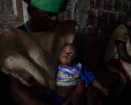 A man carries a baby, who is wearing a purple top