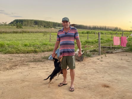 A man stands in a yard with washing visible on a line. A eucalyptus plantation is in the background.