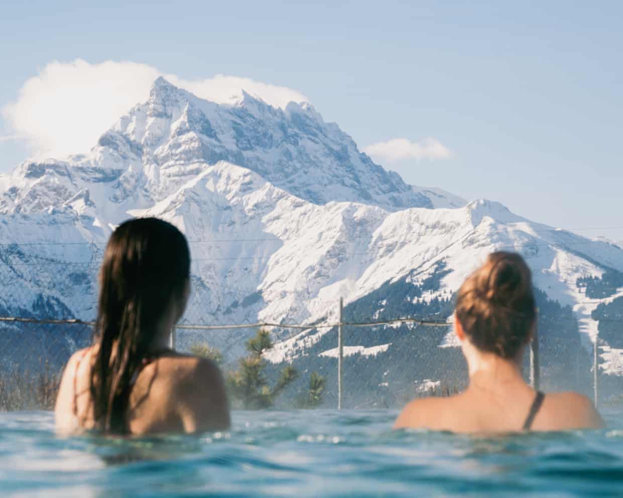 Two women in heated pool looking. out to dramatic snowy mountains