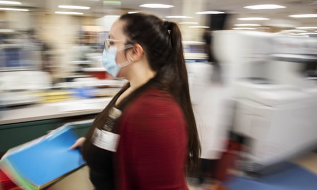 woman in surgical mask holds files in medical center - image is blurry to suggest movement