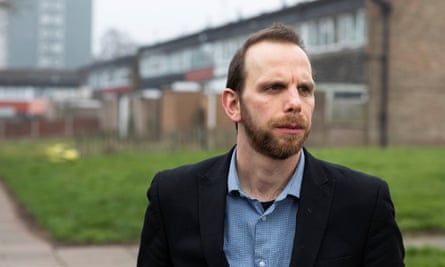 Julien Pritchard stands in front of two-storey and high-rise urban housing in a deprived area of Birmingham