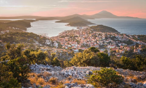 A view across houses built into the hillside, the sea and a sunset on Losinj island