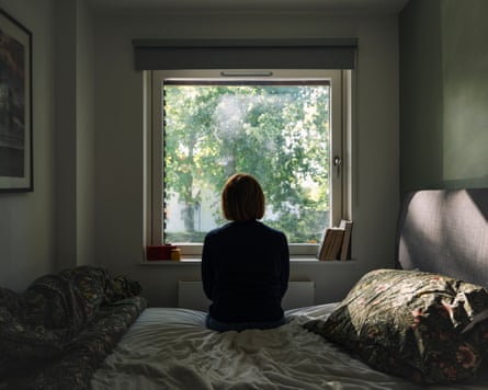 Rear view of a depressed woman looking out of her bedroom window on a sunny day