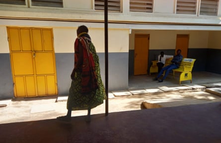 A woman walks from teh shade of a hospital building into the sunshine.