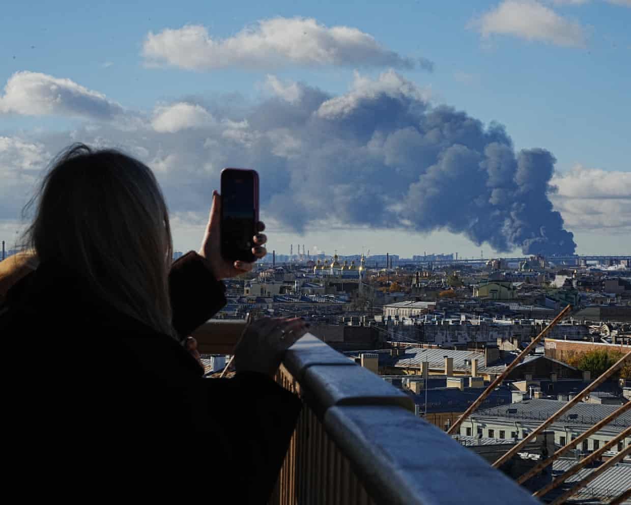 A person on a balcony takes a picture of smoke rising across the city
