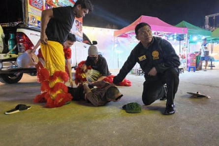 Thai police in partial costume stand over the suspect, who is lying face down and handcuffed, while a uniformed officer kneels to hold down the suspect