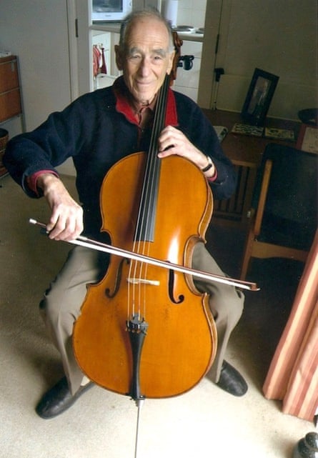 A colour portrait of an elderly man playing a cello looking straight at the camera