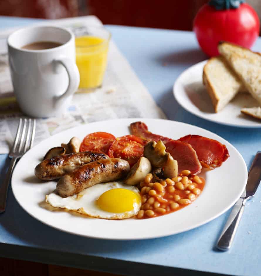 Full English Breakfast served on a cafe style blue table – eggs, bacon, sausage, beans, mushrooms and grilled tomato. Served with toast, coffee and a fresh orange.