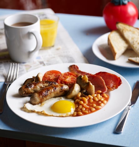 Full English Breakfast served on a cafe style blue table – eggs, bacon, sausage, beans, mushrooms and grilled tomato. Served with toast, coffee and a fresh orange.