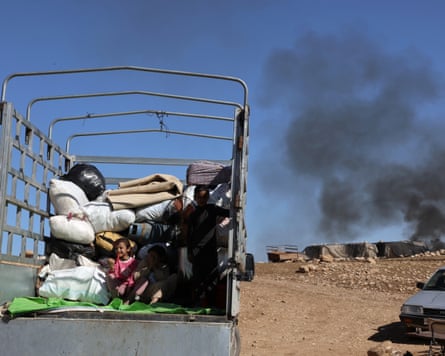 A large open truck with belongings in it with a column of black smoke in the background
