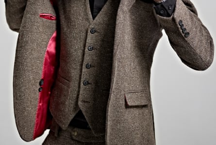 Portrait of young man in suit putting on jacket.Portrait of smartly dressed long-haired young man in brown three piece tweed suit putting his jacket on.