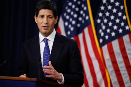 Warsh stands at a podium, with two American flags behind him