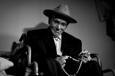 A black and white photograph of an elderly man dressed in a suit and a fedora sitting in a wheelchair.