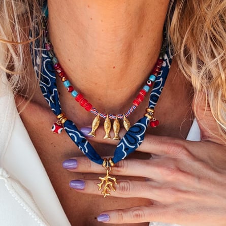A model wears a bandana woven necklace with gold branch charm. There is a shorter beaded chain with fish pendants.