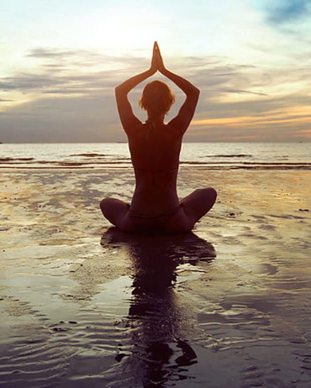A person doing yoga on a beach with their arms in the air