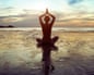 A person doing yoga on a beach with their arms in the air